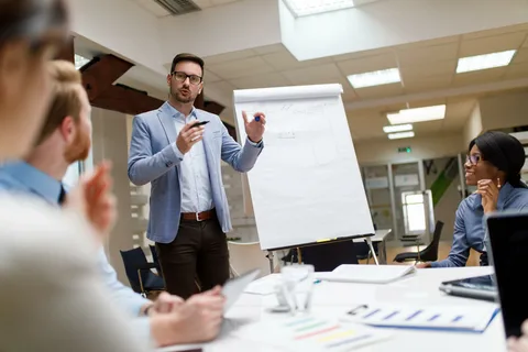 A professional meeting in a bright office, with a presenter at a whiteboard.