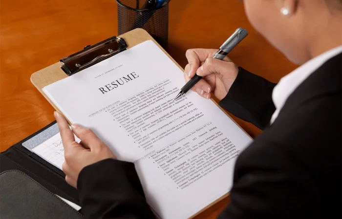 A professional woman reviews a resume on a clipboard with pen in hand