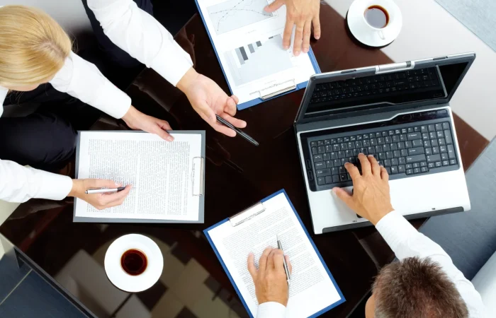 Aerial view of a business meeting with hands working on documents and a laptop