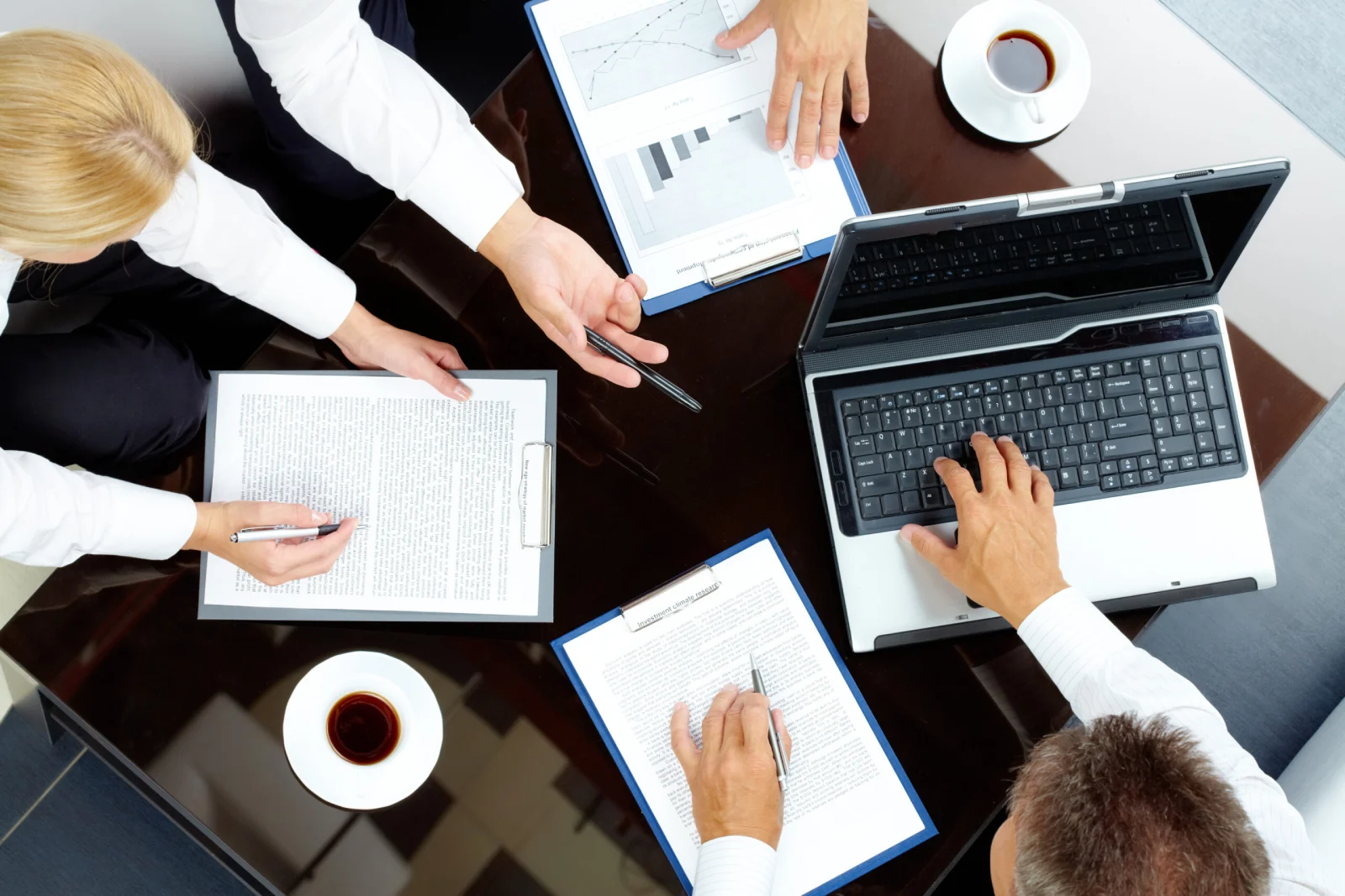 Aerial view of a business meeting with hands working on documents and a laptop